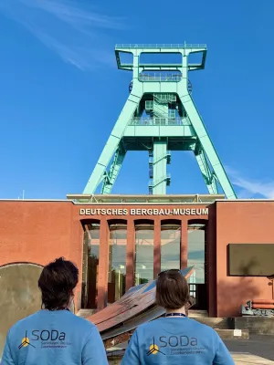 Eingang des Bergbaumuseums Bochum. Im Vordergrund zwei Personen, die man von hinten sieht. Sie tragen blaue Langarmshirts mit dem SODa-Logo auf dem Rücken.